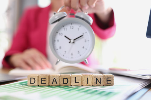Alarm clock above paperwork and wooden letters spelling deadline